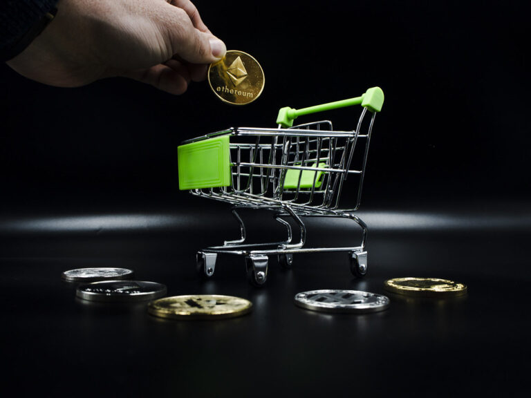 Pièces physiques représentant la cryptomonnaie Ethereum devant des graphiques de marché