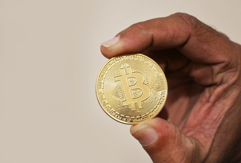 Une main tenant une piece de cryptomonnaie Bitcoin, illustrant le trading de crypto-actifs