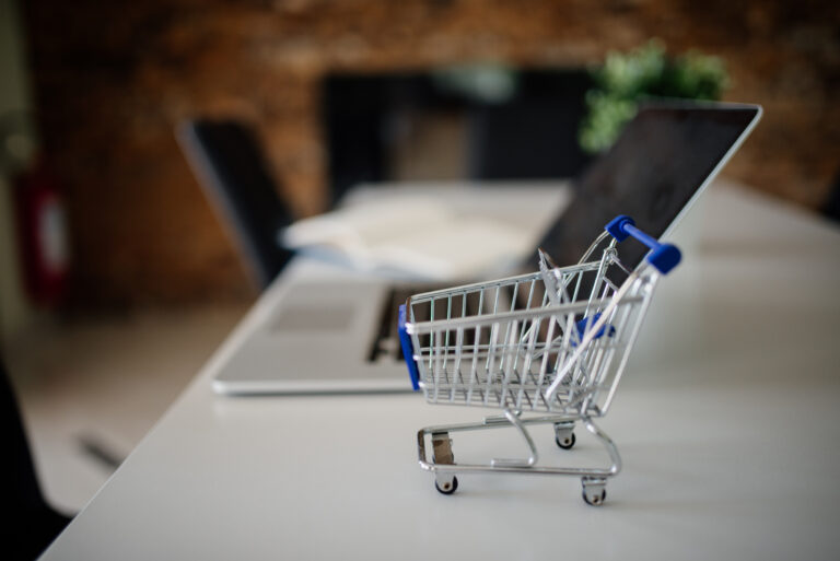 Petit chariot de courses posé sur une table à côté d'un ordinateur portable, symbole du e-commerce